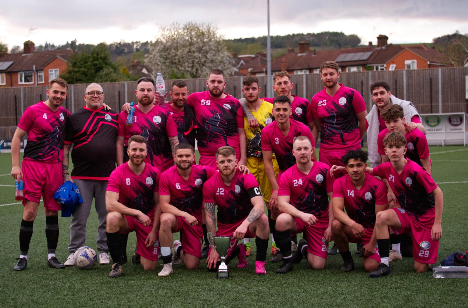 Football team in pink and black kits posing together with a trophy